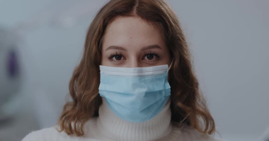 Woman wearing a blue disposable face mask looks up to the camera