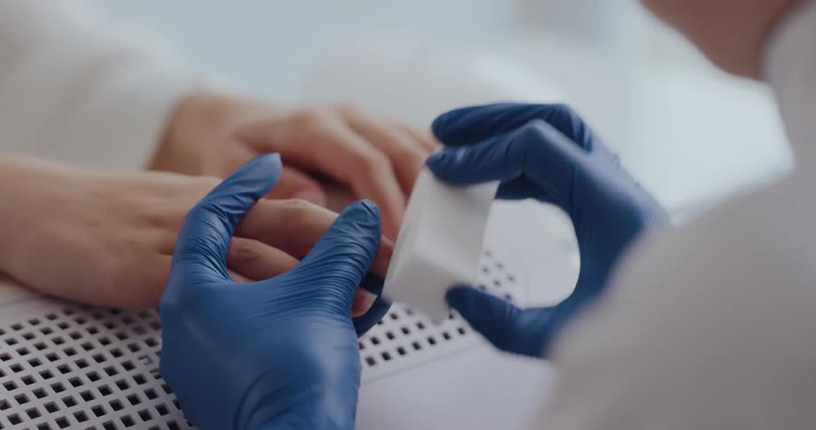 Close up of a manicurist wearing latex gloves polishing the nails of a customer