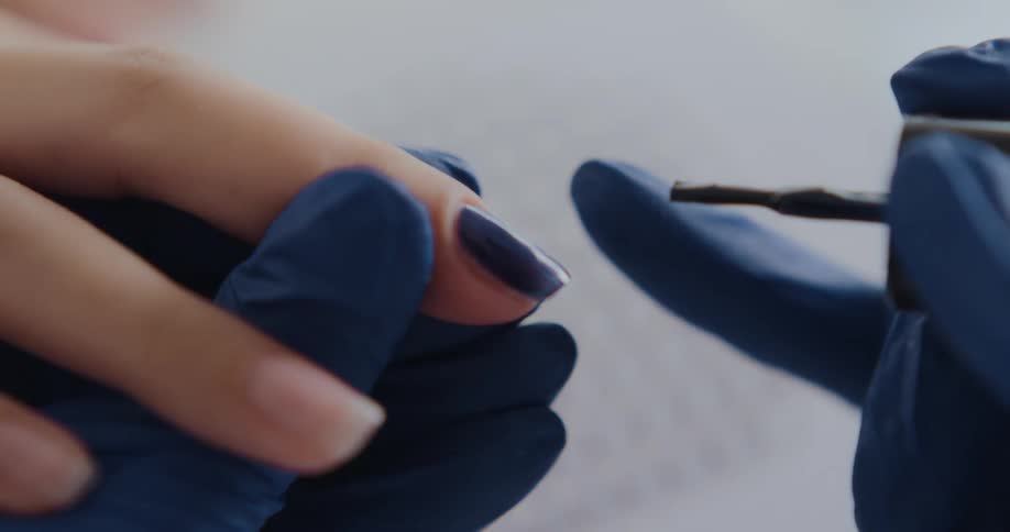 Manicurist wearing blue latex gloves applies polish on a customer nails