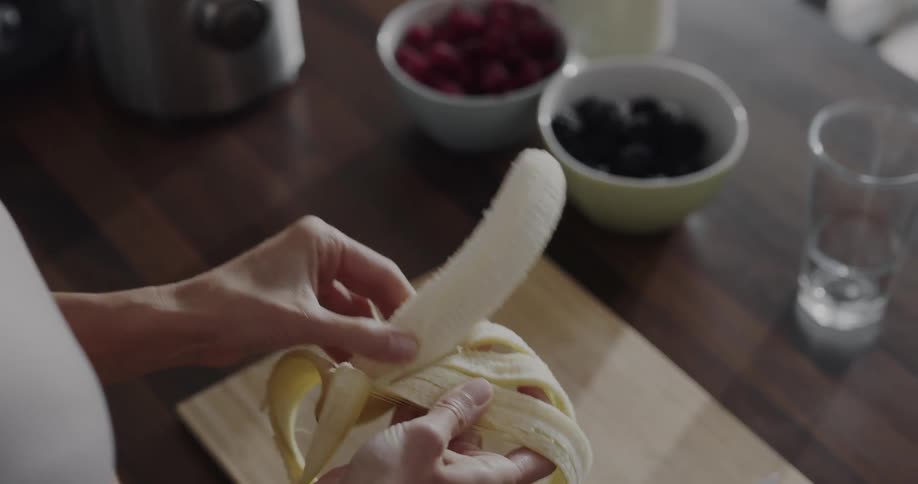 A woman puts a banana in the blender