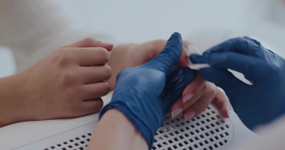 Manicurist wearing blue latex gloves cleans the nails of a client