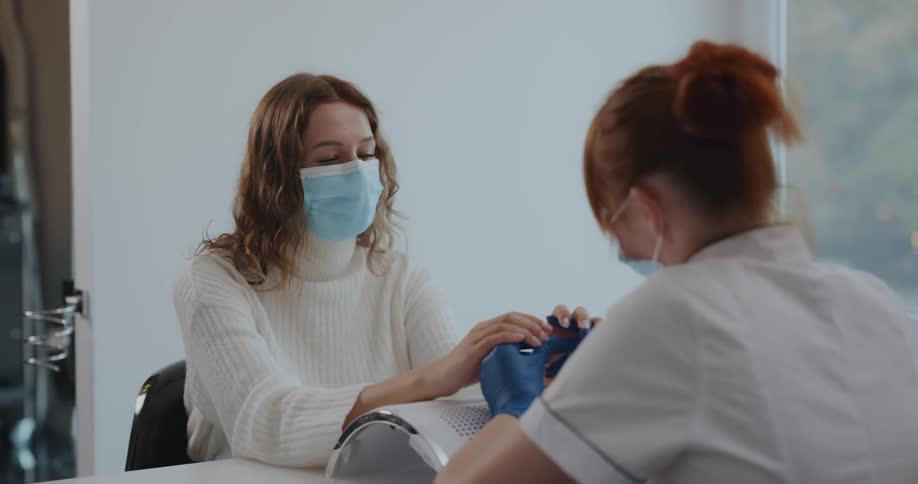 A nail technician holds a customers hands as she explains what she wants done to her nails