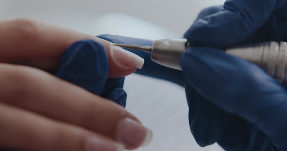 Manicurist wearing blue latex gloves trims the nails of a client
