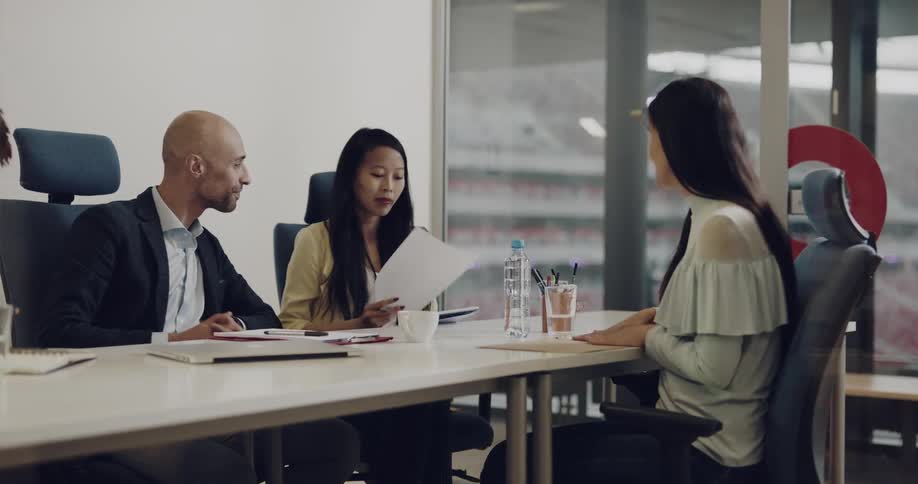 A woman passes papers to another female across an office conference table