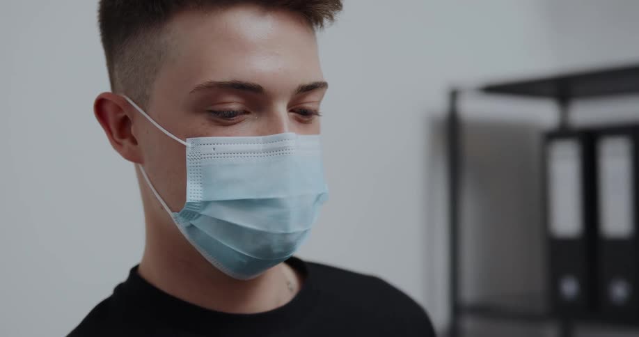 Man with blue mask and black t shirt talks to person smiling in the office