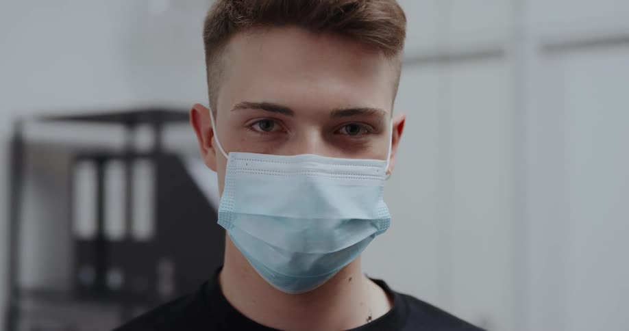 Young man wearing a blue disposable face mask looking at the camera