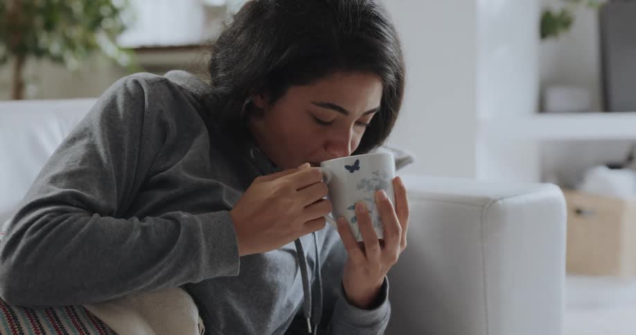 A sick woman drinks tea on the couch