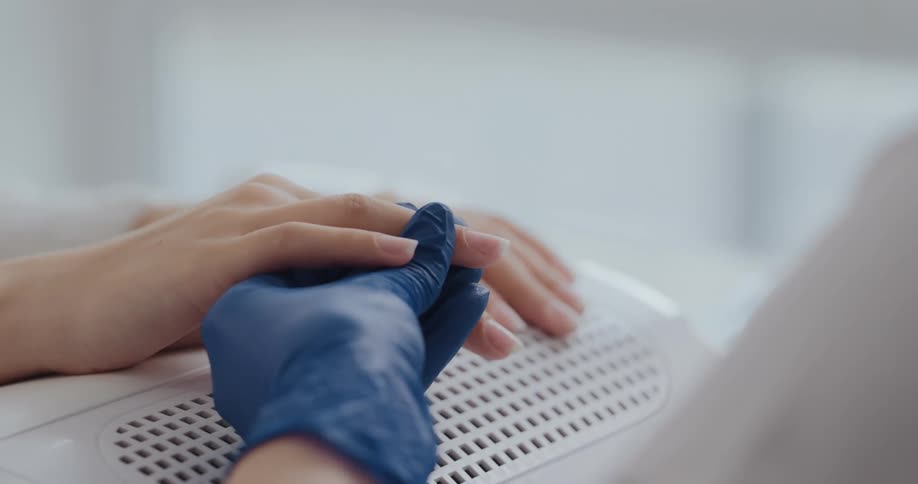 Manicurist wearing blue latex gloves applies nail polish to a client