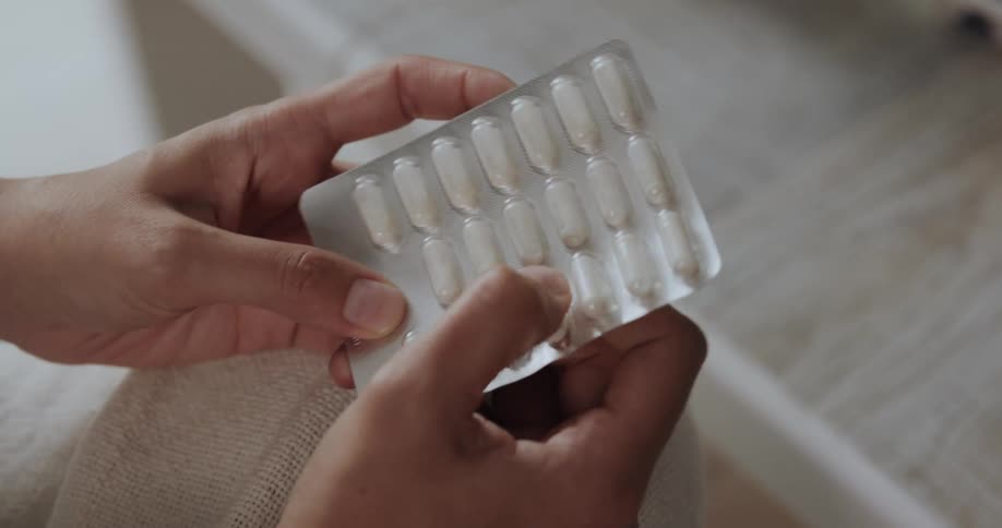A woman picks up a blister pack and pops a pill out of the foil