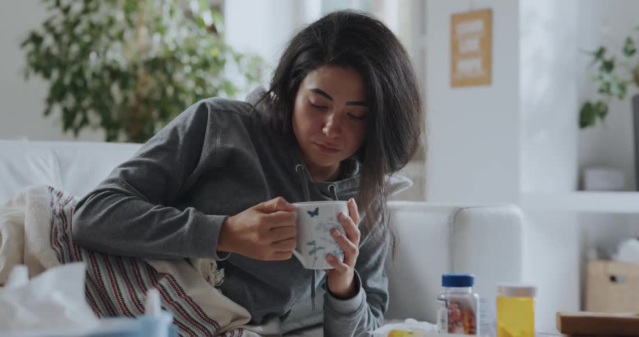 A young woman is laying on the couch and drinking coffee