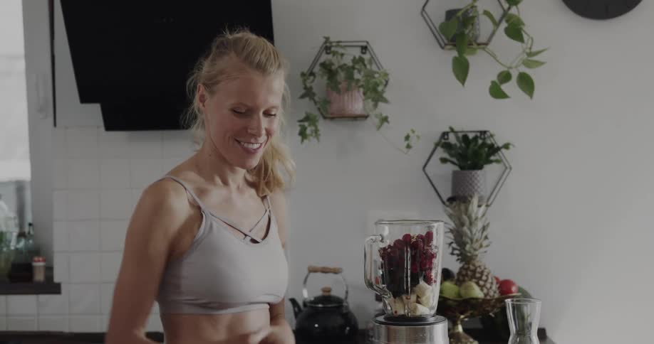 A woman pours nuts and milk into a blender filled with berries and bananas