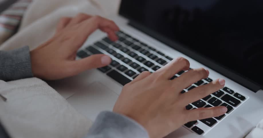 Woman sitting on the couch at home types on the keyboard of a laptop