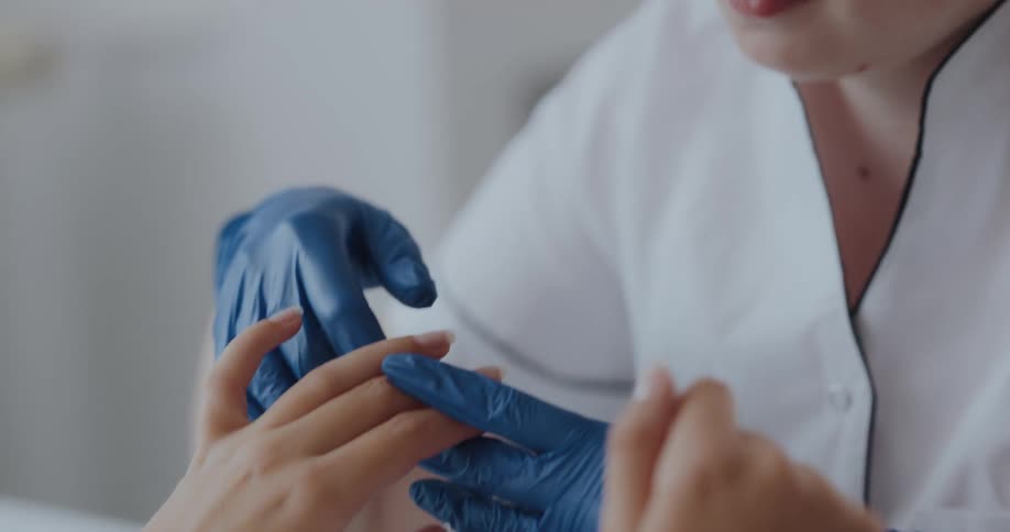 While wearing gloves redheaded manicurist examines clients hands