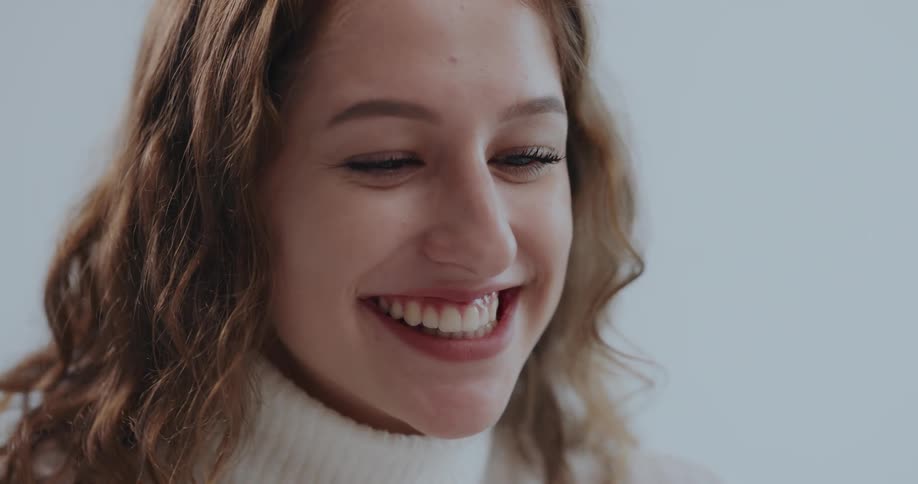 Woman with brown wavy hair and white turtleneck sweater talks to person