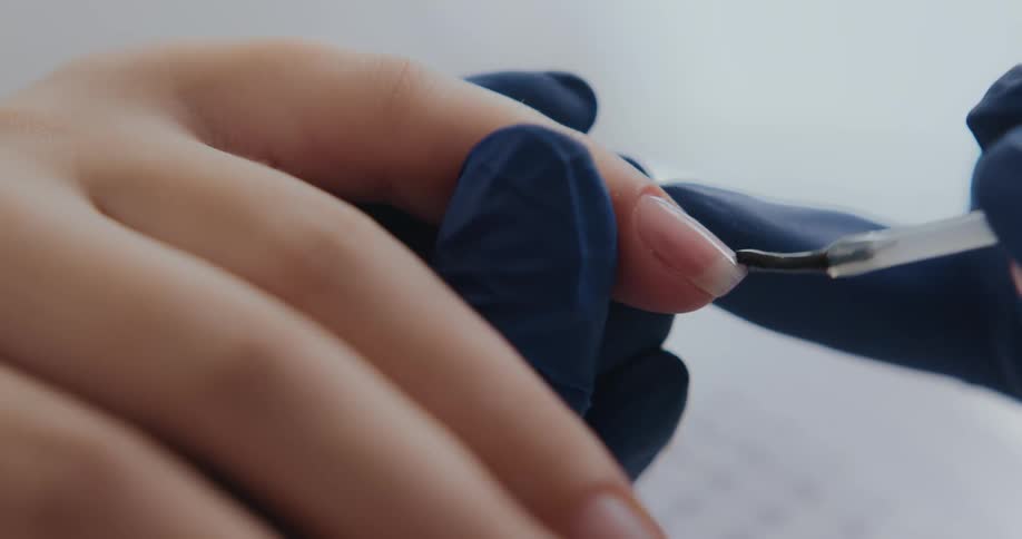 Nail technician applying clear finger nail polish on a female client