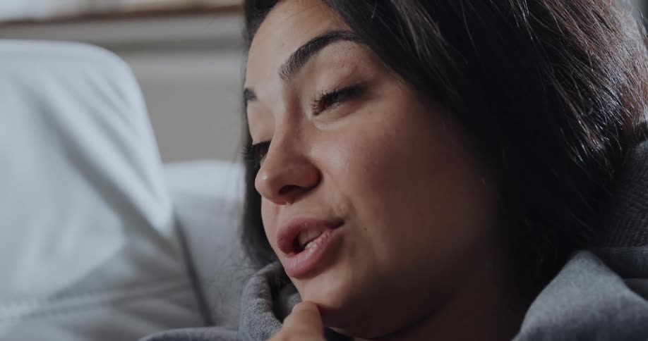 A young woman lies in bed at home and talks as she describes how she feels