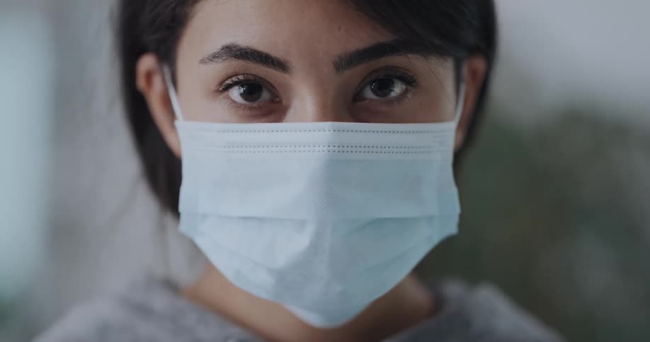 Woman looking at the camera puts on a disposable face mask