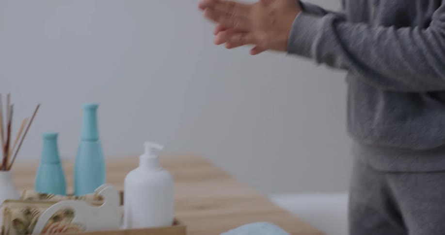 A woman approaches a table and removes her mask before sanitizing her hands using hand gel