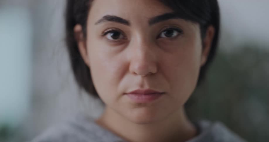 Woman wearing gray hoodie takes off blue mask and stares at camera