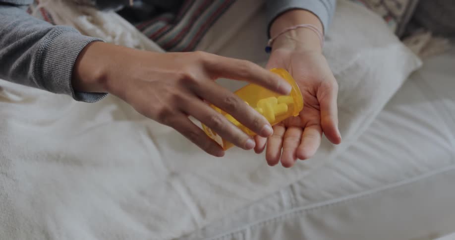 Woman picks up a medicine container and picks up one pill