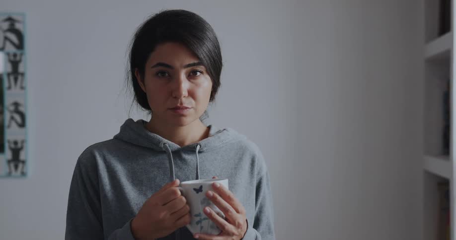 A woman is smiling and drinking a cup of coffee at her house