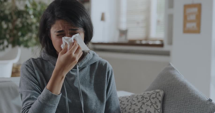 Woman sitting on couch uses nasal spray then blows her nose