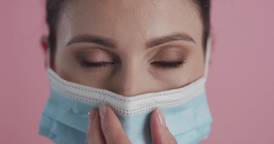 Woman puts on blue mask in front of pink wall