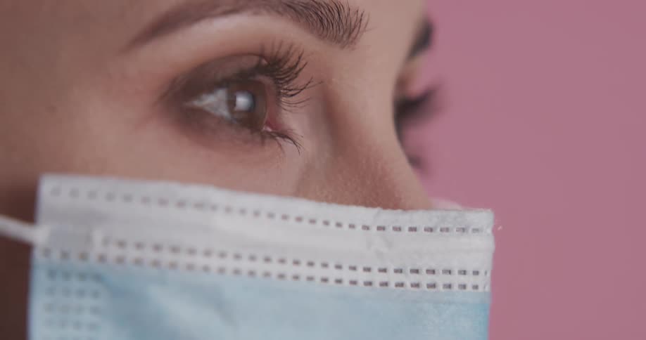 A woman puts a surgical mask on her face while staring into the distance