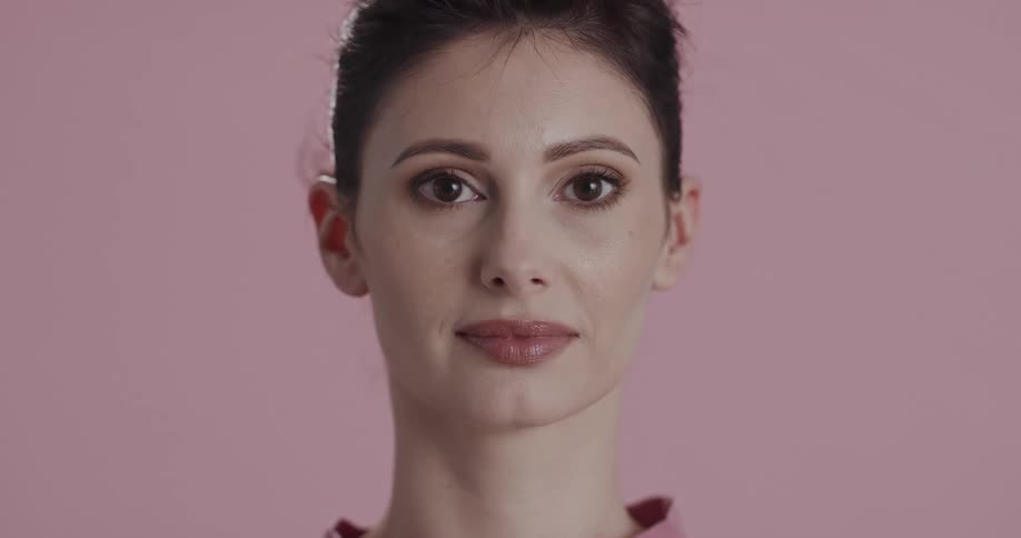 Young woman standing in front of a pink background looks at the camera