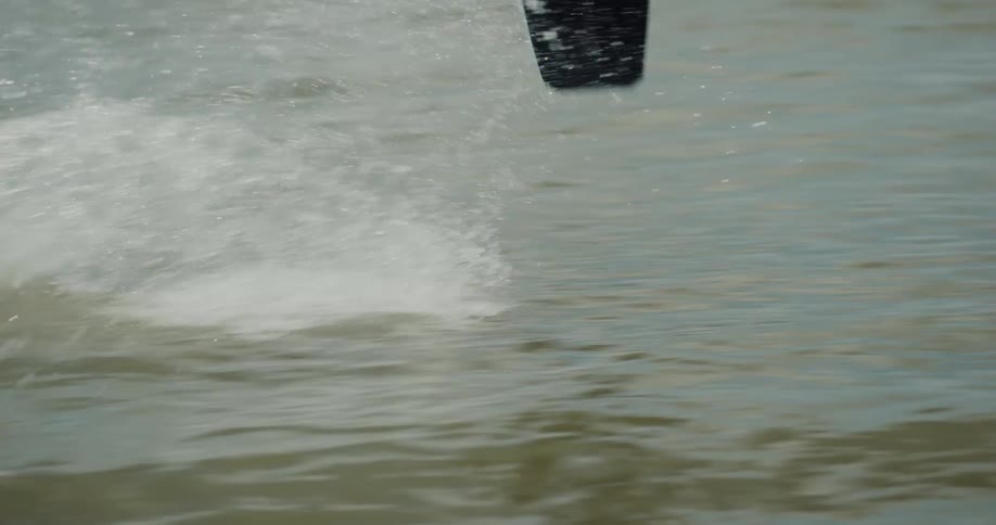 Young man rides a surfboard doing stunts on a lake pulled by a cable