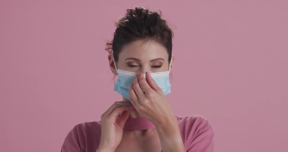 Young woman puts on a disposable blue face mask looking at the camera