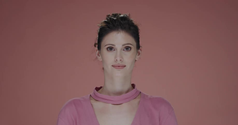 Young woman standing in front of a pink background looks at the camera