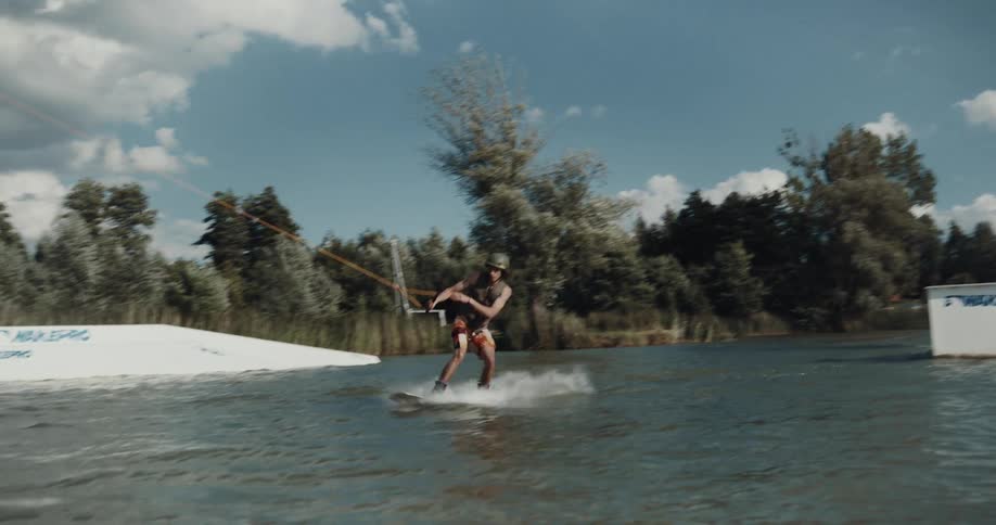 A man wakeboards off a jump in a lake rotating before splashing down