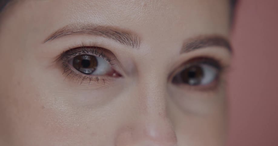 Close up of the eyes of a woman standing in front a pink background looking at the camera