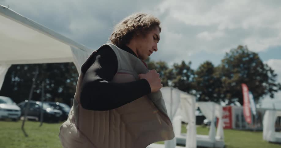 Young man wearing a wetsuit puts on a vest near a lake