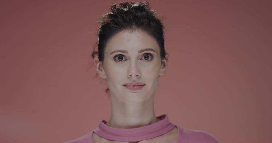 Young woman standing in front of a pink background looks at the camera