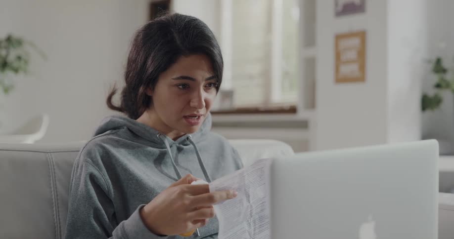 A young woman is sitting on her couch and using her laptop