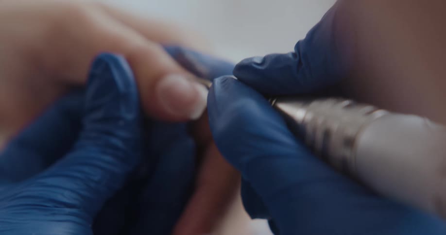 Manicurist wearing blue latex gloves trims the nails of a client