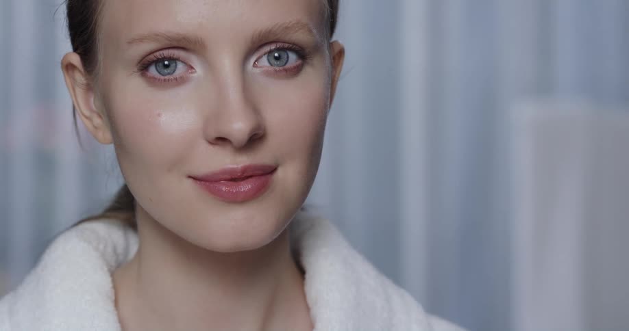 A woman in a bathrobe turns her head to smile into the camera