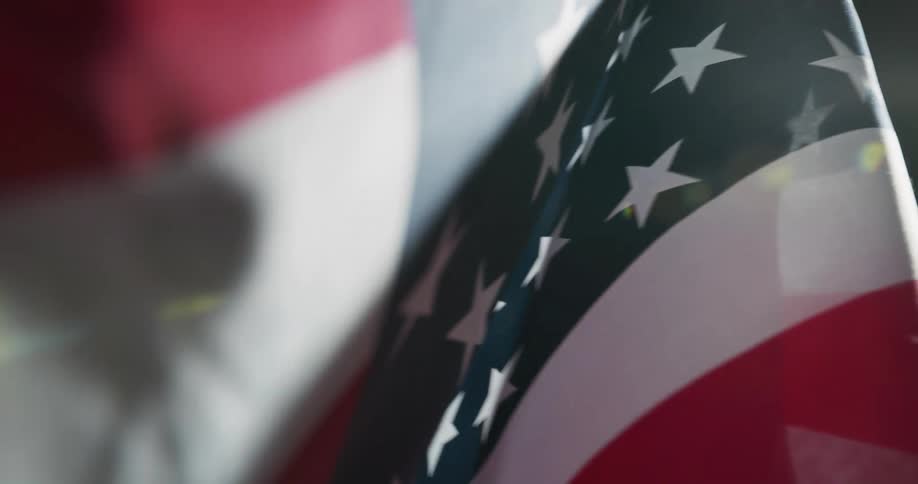 A bright light shines on an american flag waving in the wind in a dark place