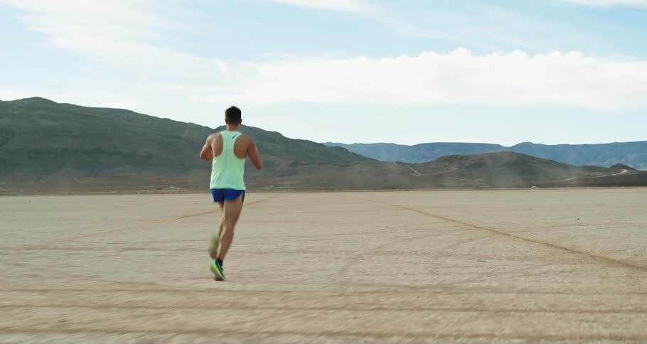Man wearing sports clothes jogging on the desert plains close to the mountains
