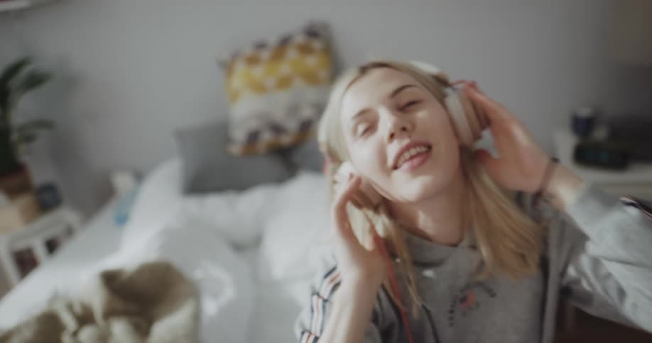 A woman dances around in her bed listening to music on headphones