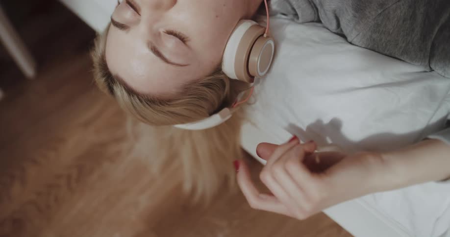 Young woman laying on bed while listening to music
