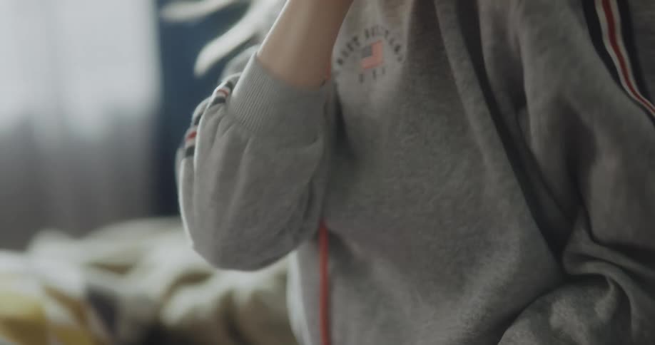 Blonde woman with gray hoodie and purple pants listens to music with headphones and dancing in bedroom