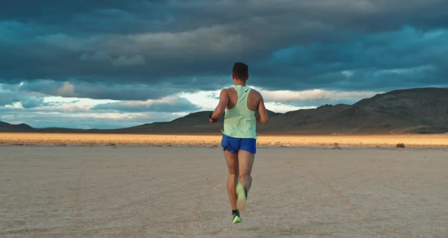 Man wearing sports clothes jogging on the desert plains close to the mountains