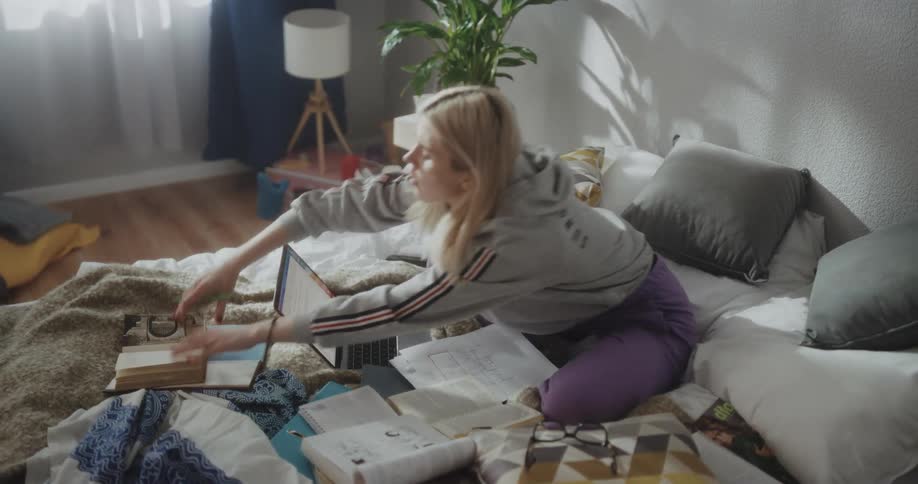 Young blonde woman sitting on the bed at home studying