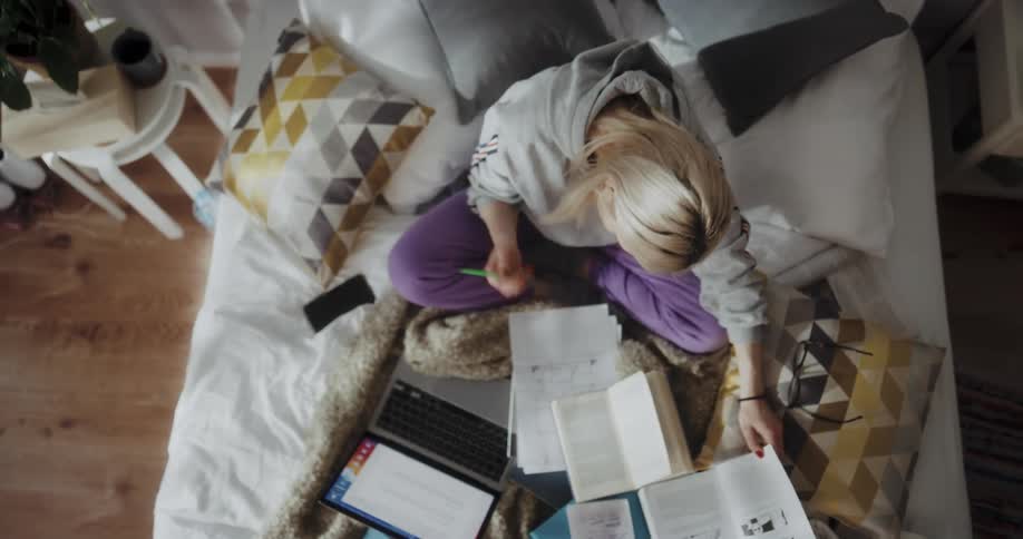 Young blonde woman sitting on the bed at home studying
