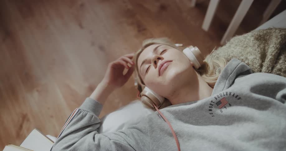 Young woman laying in bed at home listen to music in headphones