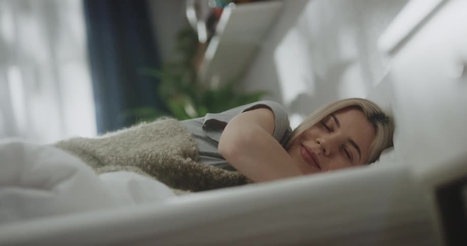 A young woman sits up and stretches after awakening in bed before climbing out