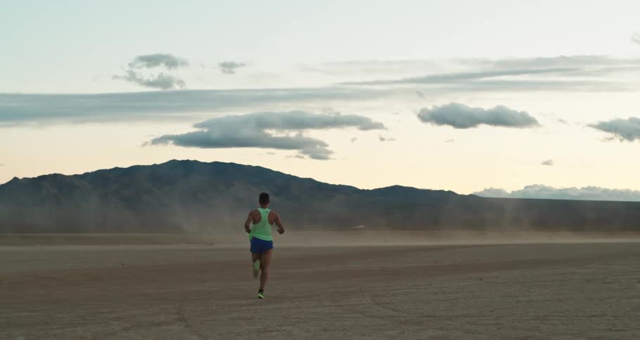A man jogs through a dusty flatland in a desert during the day